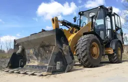 Żółta ładowarka stoi na placu budowy. Zastanawiasz się, ile zarabia operator koparki na godzinę?