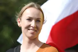 Uśmiechnięta żona Hołowni, niczym pilotka, patrzy w dal na tle biało-czerwonej flagi.