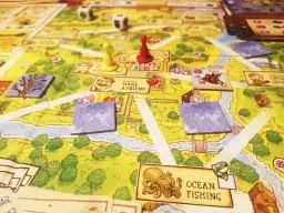 Planszowa gra Stardew Valley z pionkami, kostkami i kartami postaci. Na planszy widać rzekę, domy i pola.