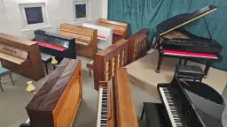 Wiele pianin i fortepianów, w tym czarny fortepian Yamaha z czerwoną wyściółką.