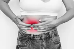 Kobieta trzyma się za brzuch, gdzie widoczny jest czerwony obszar bólu, sugerujący zapalenie trzustki objawy.