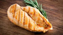 Grillowana pierś kurczaka z rozmarynem na drewnianej desce. Pytanie: ile białka ma kurczak?