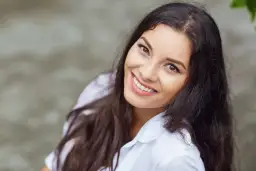 Uśmiechnięta kobieta o ciemnych włosach w białej koszuli.