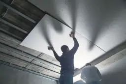 Dwóch mężczyzn montuje płyty gipsowo-kartonowe na suficie piwnicy.