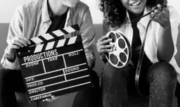 Dwie osoby trzymają klaps filmowy i rolkę taśmy filmowej. Zastanawiasz się, ile zarabia producent filmowy?