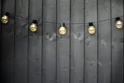 Ciepłe światło girlandy żarówkowej na ciemnej, drewnianej desce. Idealny pomysł, jaki kabel do oświetlenia ogrodu, by stworzyć przytulną atmosferę.