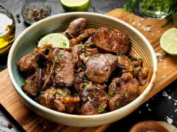 Pyszna, duszona wątróbka drobiowa z cebulką, udekorowana plasterkiem limonki. Idealna na szybki obiad, taki jak w tym przepisie na wątróbkę drobiową.