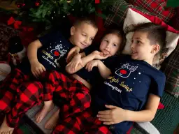 Trójka dzieci w świątecznych piżamach leży pod choinką.
