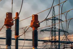 Zbliżenie na izolatory i przewody linii energetycznych. W tle widoczna wieża przesyłowa. Tabela odległości od linii energetycznych napowietrznych jest kluczowa dla bezpieczeństwa.