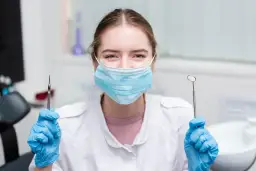 Uśmiechnięta asystentka stomatologiczna w maseczce i rękawiczkach trzyma narzędzia. Czas na egzamin!