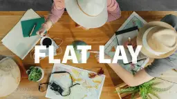 Widok z góry na stół z mapami, globusem, aparatem i notatkami. Dwie osoby planują podróż, tworząc inspirujący **flat lay**.