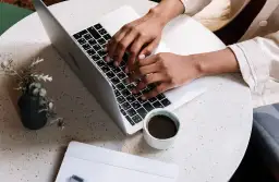 Osoba pisze na laptopie, planując, jak zarabiać na blogu. Obok kawa i notatnik.