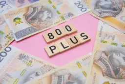 Drewniane klocki z napisem "800 PLUS" na tle polskich banknotów 200 zł.