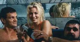 Wspólnik kilera z komedii Machulskiego, uśmiechnięta blondynka nalewa szampana, obok mężczyzna z kieliszkiem.