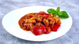 Gulasz z wołowiny z papryką, idealne mięso na gulasz. Aromatyczne danie na białym talerzu, ozdobione listkiem bazylii.