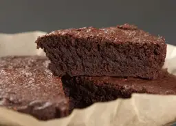 Wilgotne brownie bez jajek, posypane cukrem pudrem, ułożone na papierze do pieczenia.