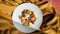 Talerz z łososiem, awokado, pomidorkami i nachos na złotym tle.