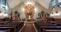 Wnętrze kościoła z ołtarzem głównym, ławkami i witrażami. Warto wiedzieć, jak się pisze "Szczęść Boże", gdy wchodzi się do takiej świątyni.