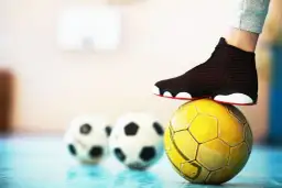 Stopa na żółtej piłce, w tle dwie białe. To pytanie: futsal co to?
