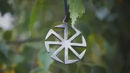 Metalowy symbol Słońca, jeden z wielu symbole słowiańskie znaczenie. Wisi na sznurku wśród zielonych liści.