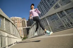 Kobieta biegnie po moście w mieście. Zastanawiasz się, ile kilometrów trzeba przebiec, żeby spalić 1 kg?