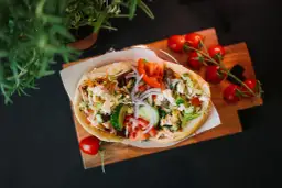 Pyszny kebab z warzywami i serem feta na desce, obok pomidorki i zielenina.