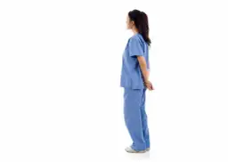 Pielęgniarka w niebieskim uniformie stoi tyłem, z rękami splecionymi za plecami. Czyżby popełniła jakiś błąd pielęgniarki?