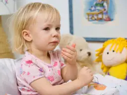 Mała dziewczynka w łóżku, otoczona pluszakami, może mieć zapalenie oskrzeli objawy.