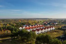 Osiedle domów z czerwonymi dachami, otoczone drzewami. Zdjęcia z drona ukazują jesienny krajobraz.