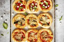 Gotowe ciasto na pizzę z różnymi dodatkami: pomidorami, serem feta i bazylią lub karczochami i szpinakiem.