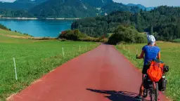 Kobieta na rowerze z bagażem na czerwonej ścieżce rowerowej. Piękna trasa Velo Dunajec z widokiem na jezioro i góry.