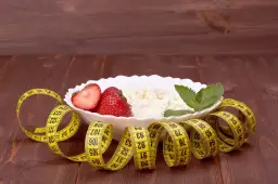Twarożek z truskawkami i miętą, otoczony miarką krawiecką. Idealne śniadanie, gdy zastanawiasz się, ile kalorii na śniadanie przy odchudzaniu.