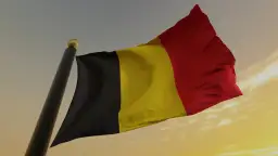 Flaga Belgii powiewająca na maszcie na tle zachodzącego słońca.