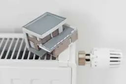 Model domu na grzejniku symbolizuje wysokie koszty ogrzewania i potrzebę dopłat do prądu.