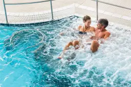 Para relaksująca się w jacuzzi, para uśmiecha się do siebie.