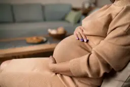 Kobieta w ciąży, z dłońmi na brzuchu, odpoczywa na kanapie. Czas na zwolnienie lekarskie w ciąży.