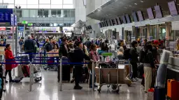 Kolejka ludzi z bagażami przy stanowiskach odprawy na lotnisku.