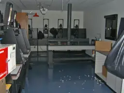 Wnętrze ciemni fotograficznej z kilkoma powiększalnikami, stołem laboratoryjnym i zlewem.