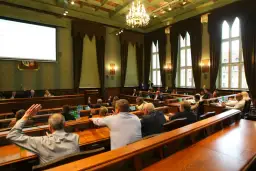 Sala obrad z ludźmi podnoszącymi ręce, widok zza pleców uczestników.