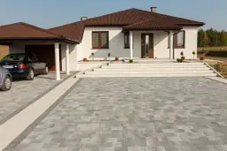 Nowoczesny podjazd z szarej kostki brukowej, idealnie komponuje się z białym domem i brązowym dachem.