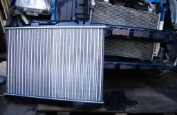 Nowa chłodnica samochodowa obok starej, zamontowanej w aucie.