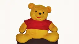 Pluszowy Kubuś Puchatek w czerwonej koszulce siedzi na ciemnym tle.