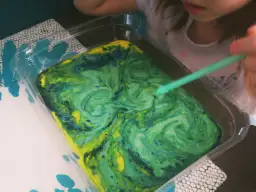Dziecko tworzy wzory na mleku, mieszając farby. Kolorowe plamy tworzą wiry.