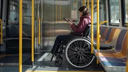 Kobieta na wózku inwalidzkim w autobusie, obok niej tablica informacyjna, która wyjaśnia, co oznaczają symbole na legitymacji osoby niepełnosprawnej.