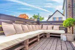 Wygodny taras z palet z beżowymi poduszkami, idealny na letnie wieczory.