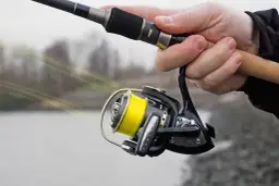 Hand hält Angelrute mit gelber geflochtener Schnur auf Rolle.