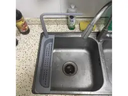 Szary uchwyt na gąbkę do zlewu, obok butelki z płynem i gąbki.