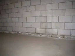 Ściana z bloczków betonowych, gdzie zaprawa murarska do bloczków betonowych tworzy solidne połączenie. Podłoga betonowa.
