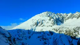 Ośnieżony szczyt Kozi Wierch zimą, z ciemnymi skałami przebijającymi się przez śnieg, na tle błękitnego nieba.