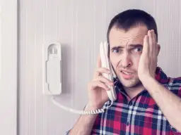 Zaskoczony mężczyzna trzyma słuchawkę domofonu, zastanawiając się, jak korzystać z domofonu.